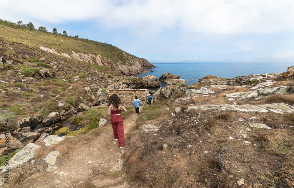 photos off the coast of Galicia, Spain. Two women with the sea and some old mills going down a cliff
