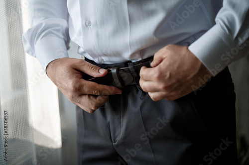 Elegant businessman man fastening a belt on his trousers he is wearing a white dress shirt