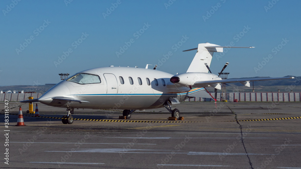 Side view of white business airplane with twin turboprop engines mounted in pusher configuration. Blue sky over the airport. Modern technology in fast transportation, business travel and tourism. Side view of white business airplane with twin turboprop engines mounted in pusher configuration. Blue sky over the airport. Modern technology in fast transportation, business travel and tourism.