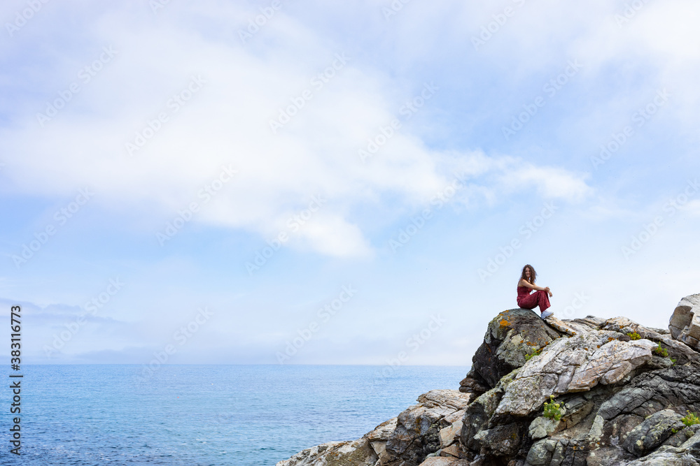Obraz premium general shot of the Galician coast with a woman perched on some rocks observing the horizon