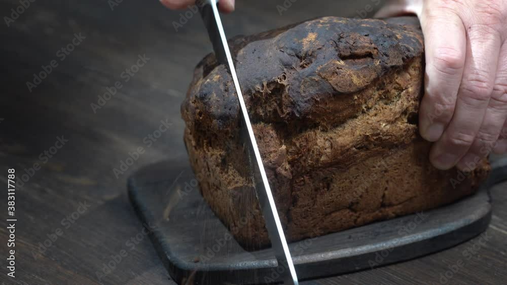 Cutting two slices of brown bread on wooden board. Cut the whole grain bread with a knife. Close up of dark bread, healthy lifestyle.