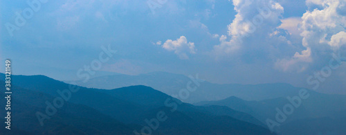 Banner of blue silhouettes of mountains in the distance, with clouds in the blue sky. Mountains and hills in the distance.