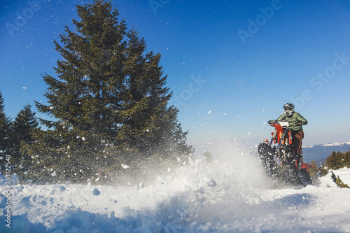 Snowbike rider in mountain valley in beautiful snow powder. Snowdirt bike with splashes and trail. Snowmobile winter sport riding photo