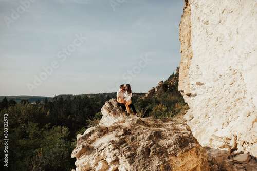 Couple travellers man and woman sitting on stones, are hugging and relaxing. Love and travel. Happy emotions. Copy space.