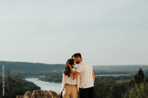 Obraz na płótnie Back view of a young stylish couple enjoying life and nature. Man embracing and kissing woman. Panorama of the mountains. w salonie