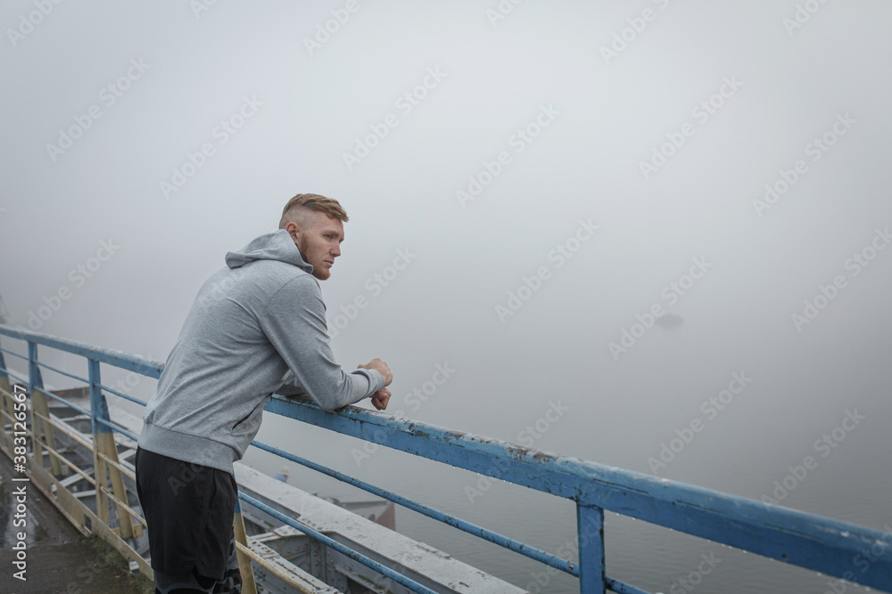 Man in gray hoodie stay on bridge in foggy morning Man in gray hoodie stay on bridge in foggy morning