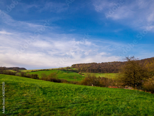 Spring landscape with a rolling meadow, forests and clouds in the sky