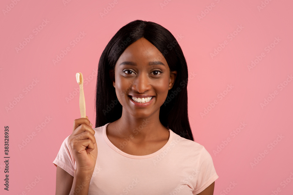 Portrait of beautiful African American woman with radiant smile holding wooden toothbrush with paste on pink background Portrait of beautiful African American woman with radiant smile holding wooden toothbrush with paste on pink background