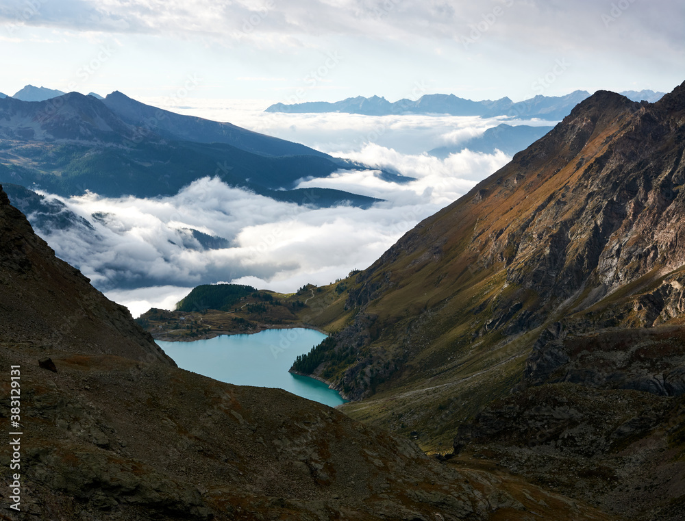 turquoise mountain lake in a crevice at dawn with solid white clouds creeping from the valley
