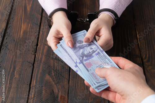 men's hands give money to women's hands in handcuffs against the background of a wooden table