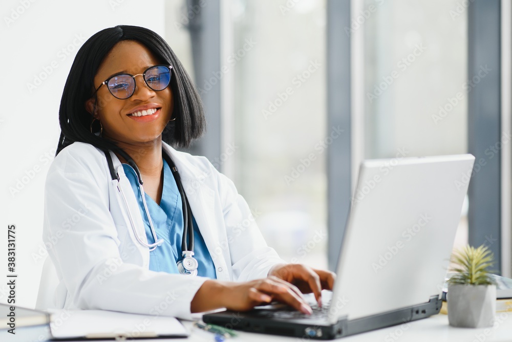 Young African-American doctor working on laptop in clinic