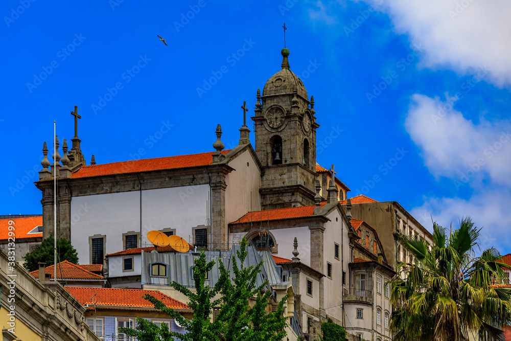 Facades and red tile roofs of traditional houses in old town, a stone church tower in the background in Porto, Portugal