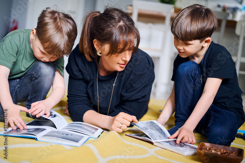 Young caucasian mother spending time at home with sons and reading books on the floor. Happy parent playing with preshool children. Home education concept photo