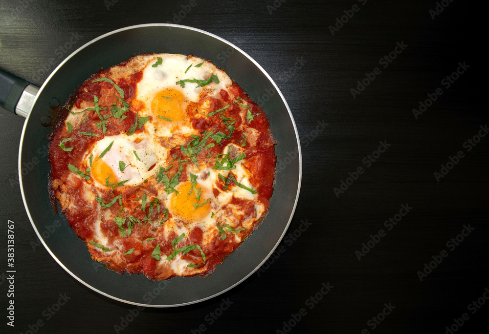 Shakshuka - poached eggs in tomato sauce, onion, pepper and spices in iron pan on dark wooden table with copy space. Famous traditional Arabic and Israeli breakfast - chakchouka. Top view