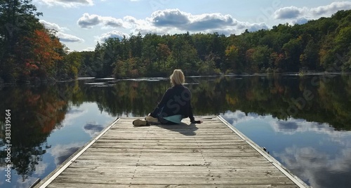 Female Sitting on the Edge of a Wooden Dock with Stunning Views of Autumn Trees and Lake Reflections