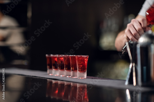 bartender pours red alcohol into shots on the bar, bartender's show.