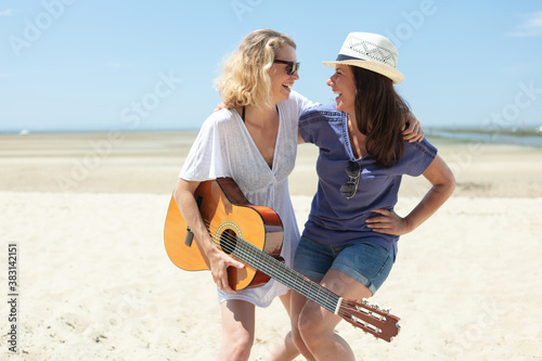 two women laughing on the beach holding a guitar © auremar