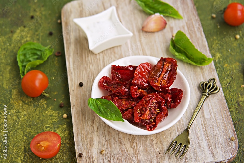 Homemade sun-dried tomatoes in a white bowl on a wooden board on an olive green concrete background. Canning, preserves. Harvest tomatoes. Homemade sun-dried tomatoes in a white bowl on a wooden board on an olive green concrete background. Canning, preserves. Harvest tomatoes.