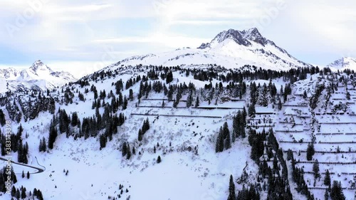 Hill in  Austria. Iced peak with snow and cloudy sky. Snow walls and trees in the front. Drone view
