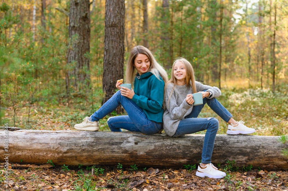 Fototapeta premium Mom and daughter have fun talking in the autumn forest. The girls are drinking tea at the picnic.