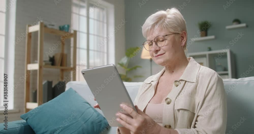 Senior caucasian lady using a tablet computer at home. Mature woman surfing web or reading news during self isolation 4k fooatge Senior caucasian lady using a tablet computer at home. Mature woman surfing web or reading news during self isolation 4k fooatge