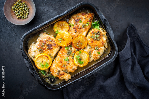 Traditional Italian deep-fried chicken piccata with capper and lemon slices offered as top view in a rustic old roasting pan with copy space photo