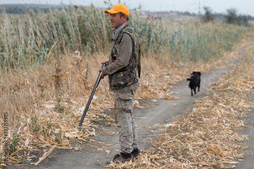 Duck hunter with shotgun walking through a meadow.