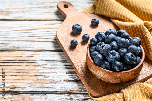 Ripe blueberries in a wooden bowl. White wooden background. Top view. Copy space