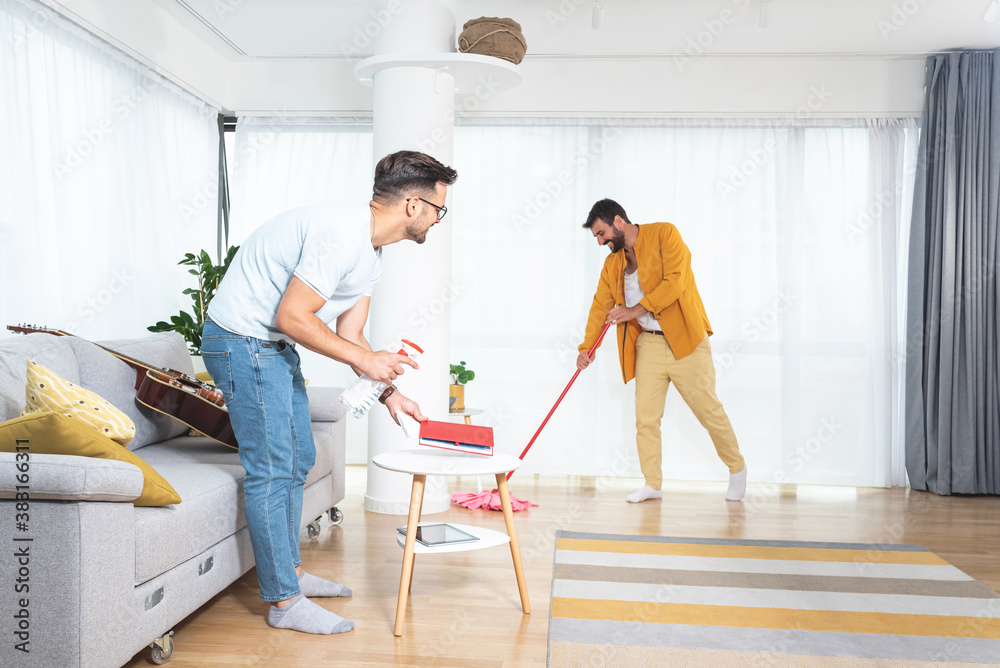 Gay couple cleaning living room with mop and spray bottle
