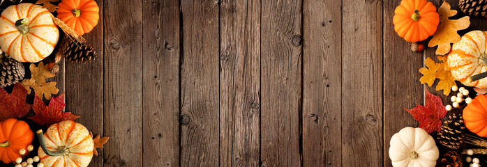 Natural autumn double border of pumpkins and leaves. Top view on a rustic dark wood banner background with copy space.