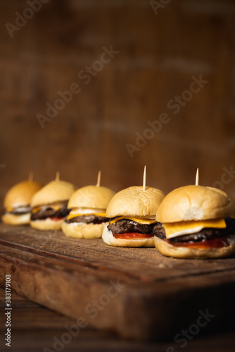 Homemade mini burguers made of ground beef, cheddar cheese, tomato and mayonnaise on a wooden table with a brown raw wooden background and space for text.  photo