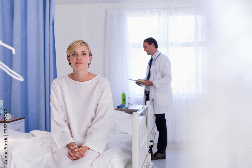 Fototapeta premium Portrait serious young female patient sitting on edge of hospital bed