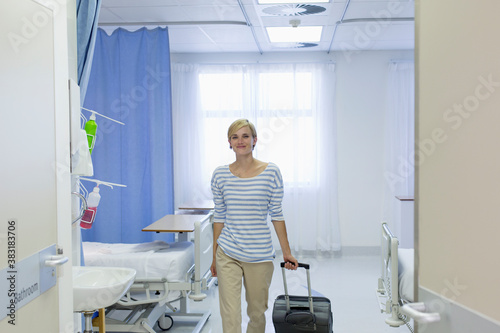 Fotografie Smiling female patient with suitcase leaving hospital room