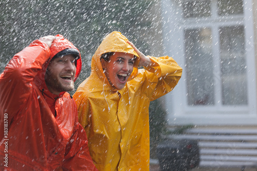 Schilderij op canvas Happy couple in raincoats walking in rain