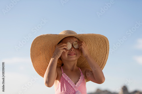 Vászonkép Portrait cute girl in sun hat covering eyes with seashells