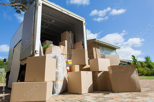 Cardboard boxes outside moving van and house in sunny driveway
