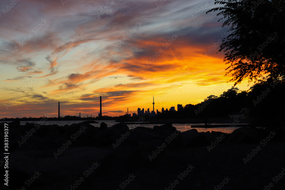 Sunset in city Toronto. Darkness cityscape and golden hour.
 Blue and yellow colors cloudy sky and lake Ontario