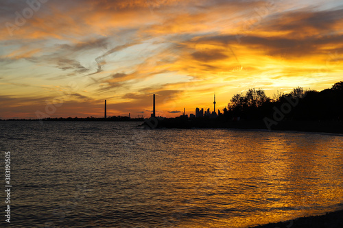 Sunset in city Toronto. Darkness cityscape and golden hour. Blue and yellow colors cloudy sky and lake Ontario
