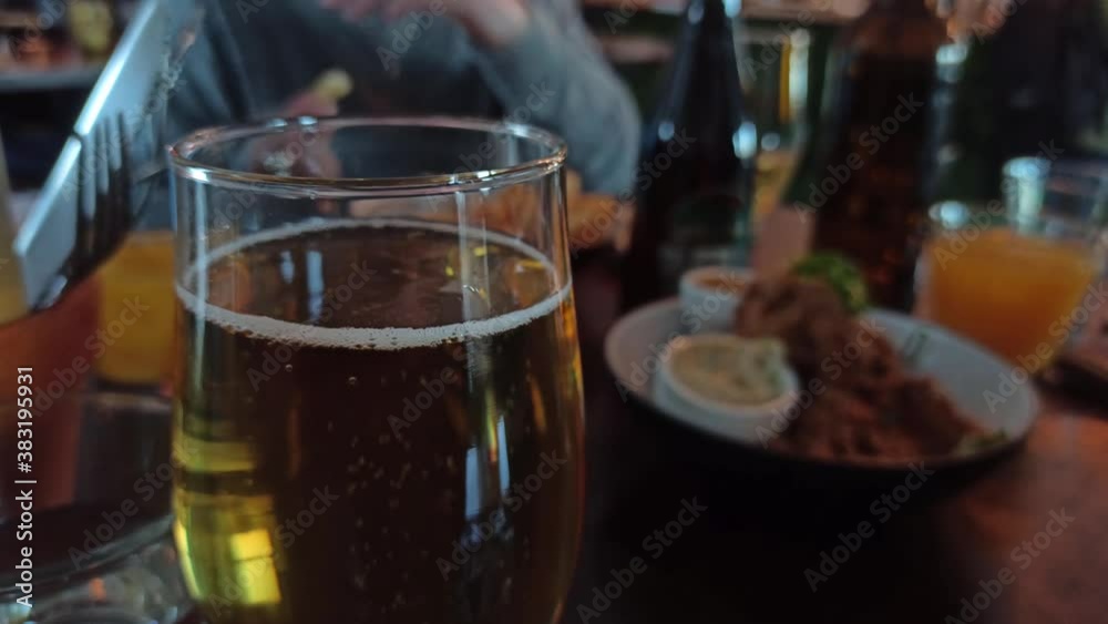 A close up shot of a glass of cider while people grab food from plates in the background.