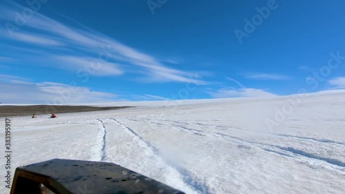 View from camera mounted on side of buggy car showing tourists enjoying motor sledging on snow covered glacier.