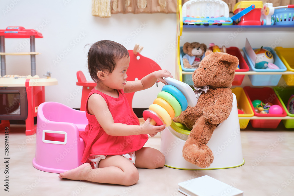 Asian toddler girl child sitting on potty and reading a book with toys ...