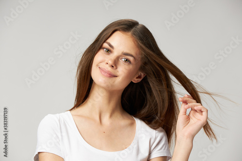 A woman in a white T-shirt touches the hair on her head with her hand on a light background 