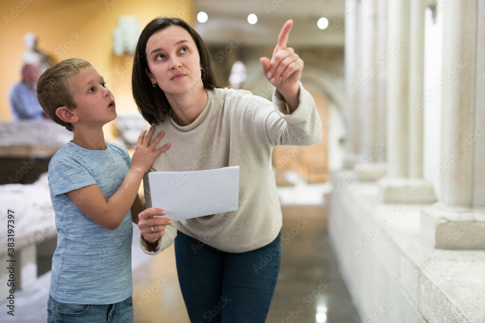 Young female tutor with boy looking at exposition in museum of ancient sculpture, pointing to something