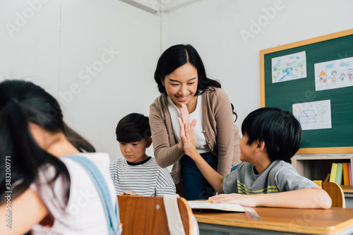Young Asian teacher giving boy high five in school, success, achievement, happiness. Asia school boy with young woman in class.
