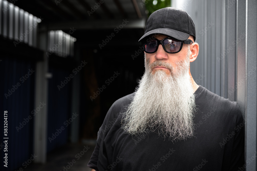 Mature bearded hipster man with cap and sunglasses thinking outdoors