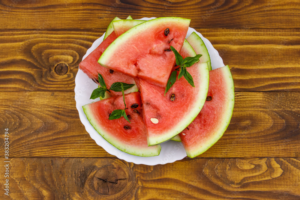 Fresh ripe sliced watermelon in white plate on a wooden table. Top view Fresh ripe sliced watermelon in white plate on a wooden table. Top view