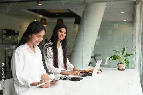 Couple of businesspeople sitting together in modern office and talking to each other on working desk.