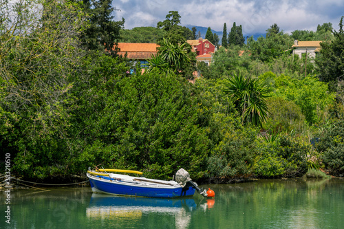 Beautiful tranquil landscape - sea bay with calm water, fisher boat, coastline - green lawns and palm trees. Corfu Island, Greece.