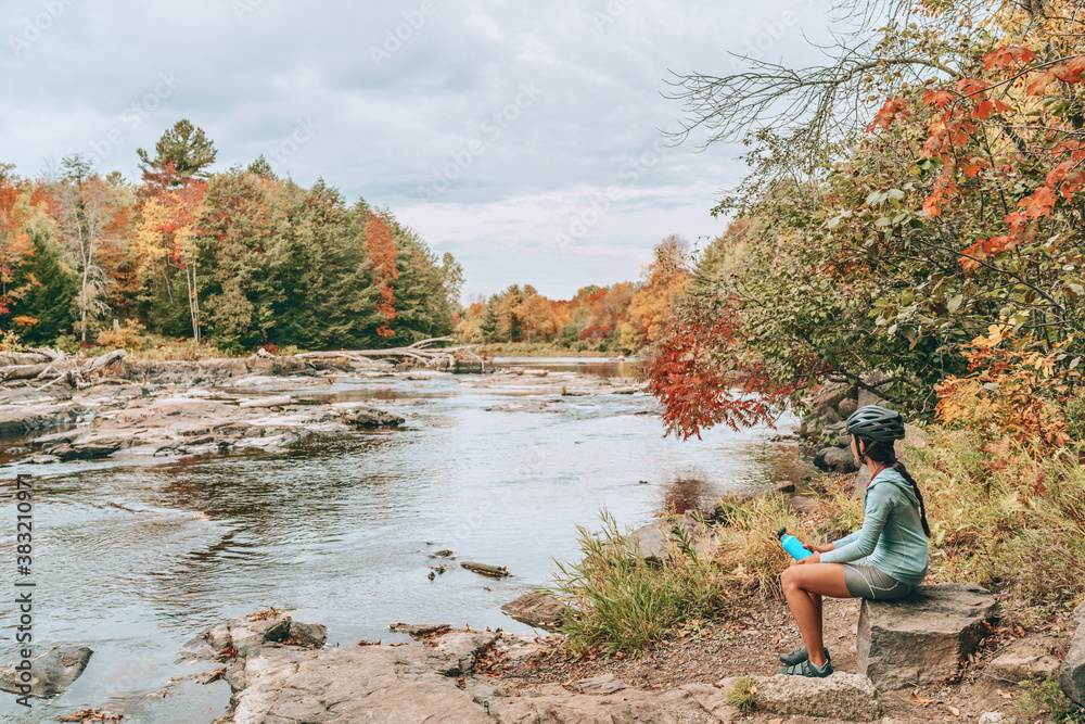 Autumn landscape woman taking a break by river during biking trip on Canada travel vacation. Fall foliage scenery view in Quebec. Autumn landscape woman taking a break by river during biking trip on Canada travel vacation. Fall foliage scenery view in Quebec.