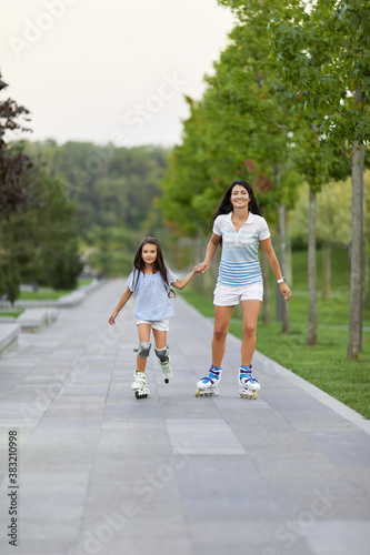 Young mother and her cute little daughter rollerskating in summer park. family concept